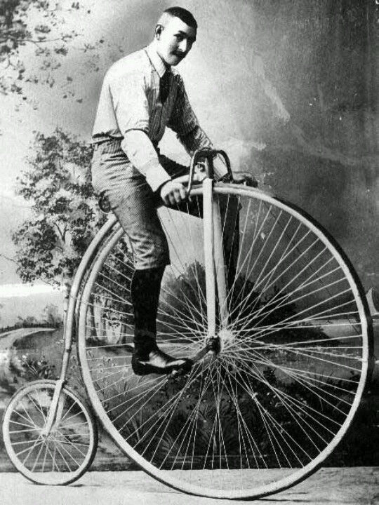 a man on a vintage bicycle with a very high seat